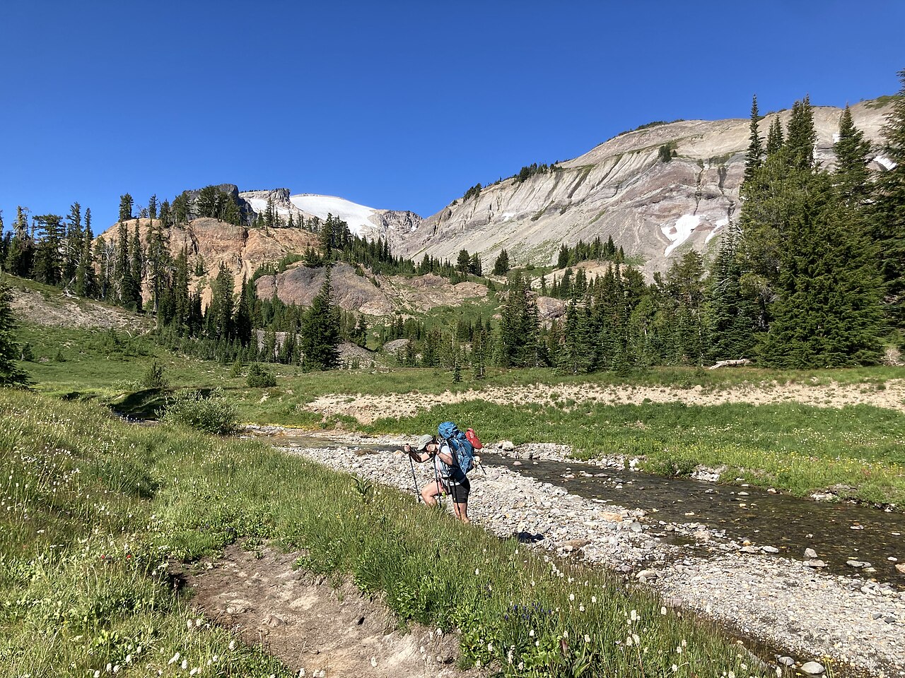 Randonneur traversant un ruisseau en montagne pour illustrer une micro-aventure nature.