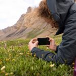 Randonneuse photographiant des fleurs sauvages avec son smartphone sans quitter le sentier.
